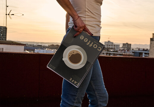 Real photo of woman Holding a front cover Sketchbook at Sunset on a Roof. PSD mockup