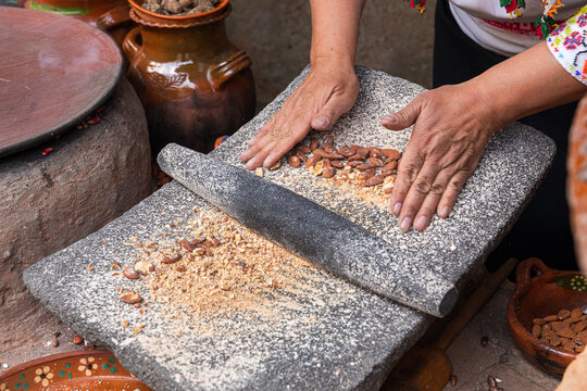 Hands rolling stone over crushed almond mixture in a metate