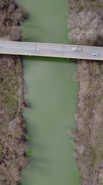 Vertical aerial top down view of a murky green river crossed by a bridge in winter - early spirng