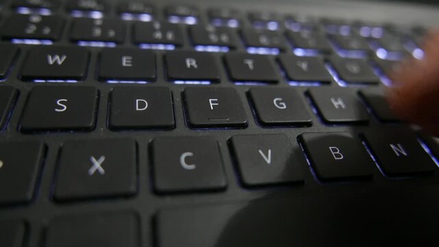 POV of someone typing on a laptop backlit keyboard. A close-up shot of a computer keyboard. A man writing on a laptop. Someone typing with one hand. Computer keys.