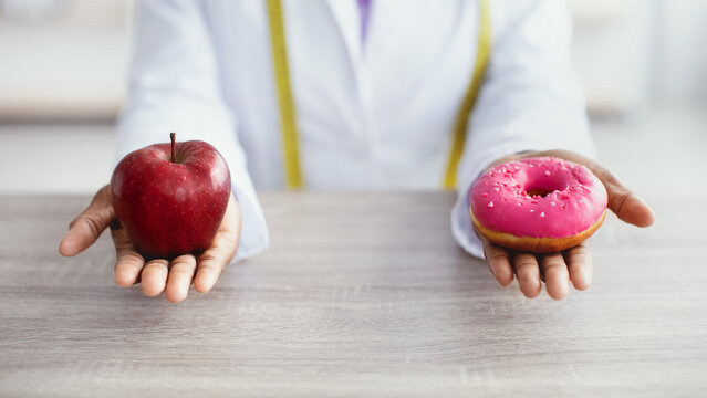 A person holds an apple in one hand and a pink frosted donut in the other hand in a setting focused on health choices. The activity highlights the contrast between healthy and unhealthy options.