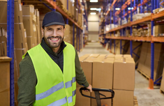 Worker in warehouse moves pallet with trolley. Boxes on shelves, manual jack moving goods for logistics, shipping, and inventory. Efficient warehouse operations and strong teamwork concept.