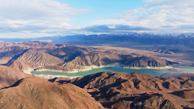 Aerial view captures a serene Orto Tokoy reservoir nestled among majestic snow-capped mountains in Kyrgyzstan. Cloudy sky adds to the peaceful, isolated atmosphere.