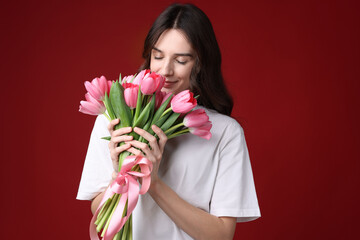Young woman sniffing bouquet of pink tulips on dark red background