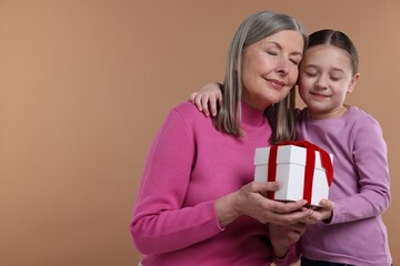 Little girl greeting her grandmother with gift on dark beige background, space for text