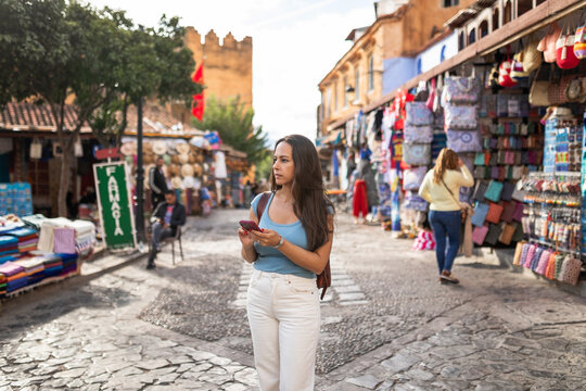Young woman checking mobile phone in medina square of Chefchaouen