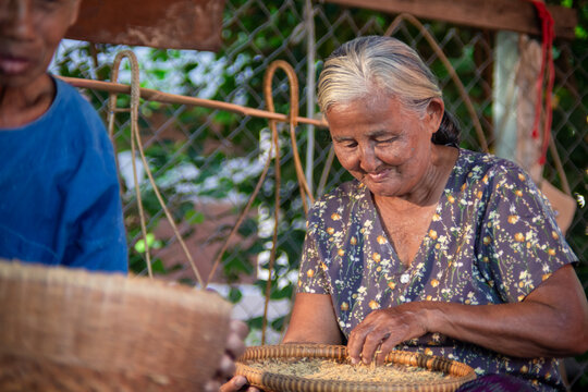 Senior Asian woman sorting rice grains as her husband crafts
