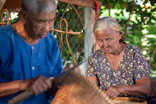 Senior Asian woman sorting rice grains as her husband crafts