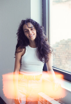 Smiling Woman With Curly Hair Standing by a Large Window
