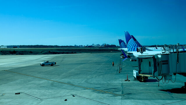 United Airlines tail fins at Nashville International Airport (BNA) with Nashville in the background. Another passenger plane is on the runway in front of Nashville. Copy space is in the image.