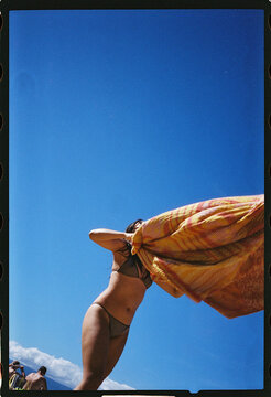Woman shaking sand off of towel at the beach 