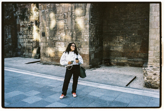 Woman Holding Coffee Stands Near Ancient Stone Wall in City