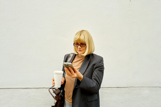 Woman Standing Against a White Wall While Checking Her Phone
