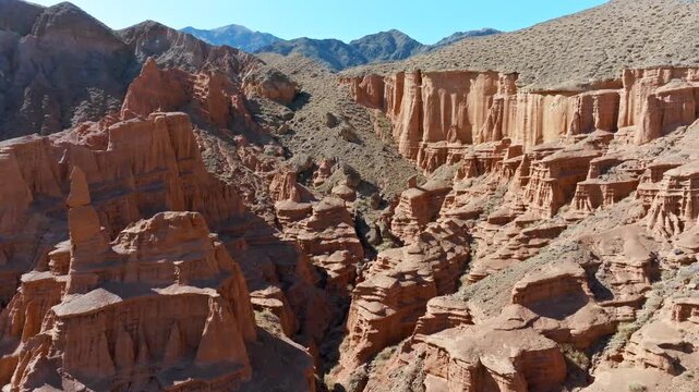 Vast desert canyon showcases stunning layered red rock formations under clear sky. Forward flying drone view.