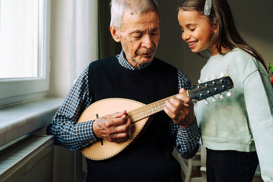 Senior man playing a mandolin to his granddaughter