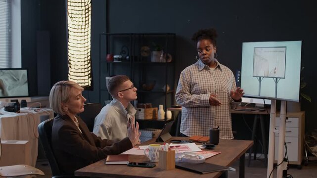 Photo crew gathering in studio to discuss commercial photo shootings together, African American woman presenting photo references