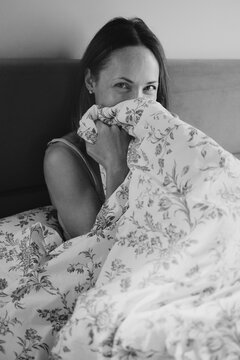 Woman playfully hiding behind a patterned duvet in a cozy bedroom
