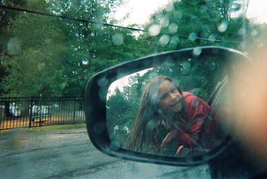 Girl in reflection of car rear view mirror in the rain