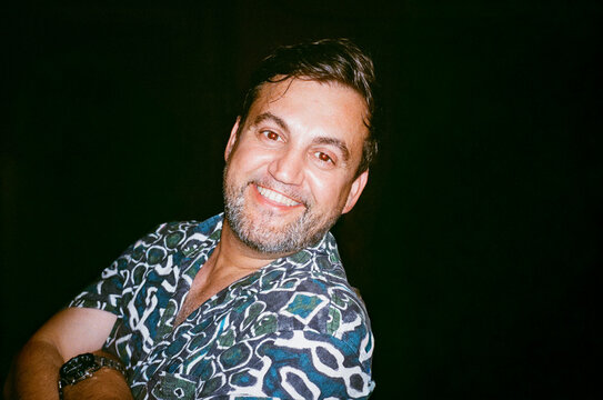Man Smiles Warmly at the Camera While Wearing a Patterned Shirt
