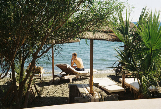 Relaxing by the Beach Under a Thatched Umbrella on a Sunny Day