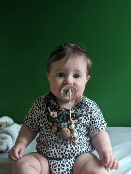 Baby with a pacifier in front of a green wall