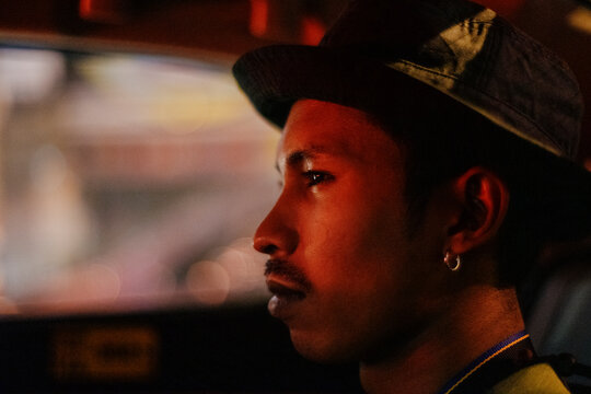 A young man sitting in a vehicle at night in dim light