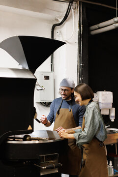Young smiling workers controlling process of coffee roasting
