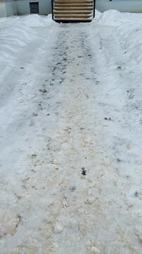A snow-covered unmade path to the entrance to the pharmacy, a narrow trampled path through deep snow with sand and slush, leading iron steps.
