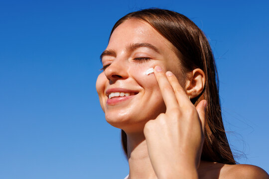 Smiling woman applies skincare in bright summer blue sky