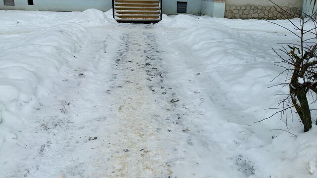 A snow-covered unmade path to the entrance to the pharmacy, a narrow trampled path through deep snow with sand and slush, leading iron steps.