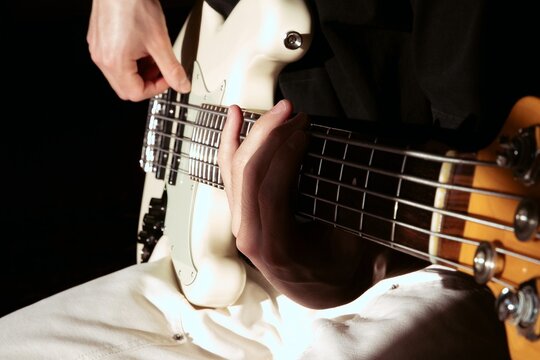 Hands Playing a White Electric Bass Guitar in Dramatic Shadow Light