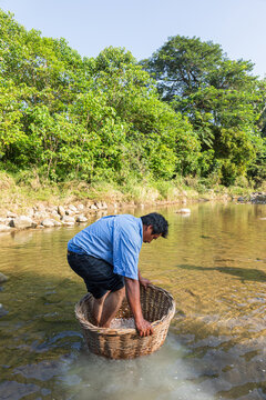 Man washing cacao with basket in clear river water