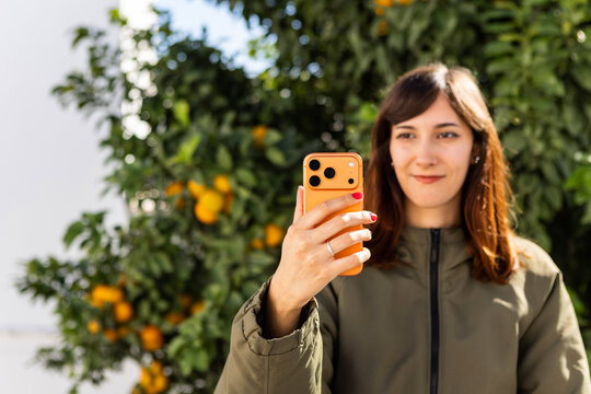 Young Woman Takes Selfie in Vibrant Orange Garden During Sunny Day