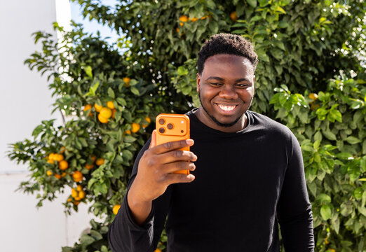 Smiling Man Using His Phone in an Orange Grove During Daylight