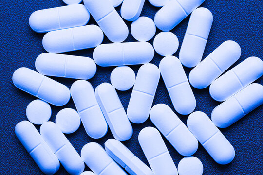 White medical tablets scattered on blue surface. Pharmaceutical pills arranged in random pattern. Healthcare and medicine concept showing solid dosage forms used for treatment, therapy, pain relief.