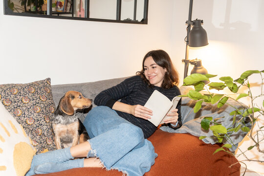 Woman Reading a Book on a Cozy Couch With Her Dog