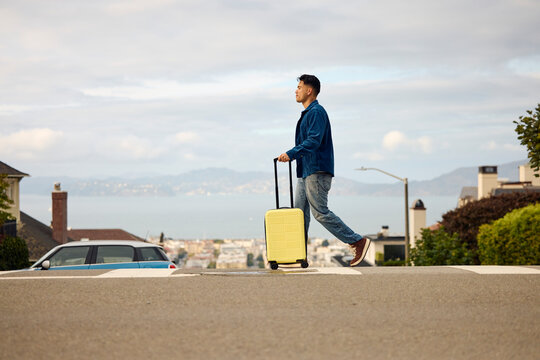 Man is crossing the street dragging a suitcase