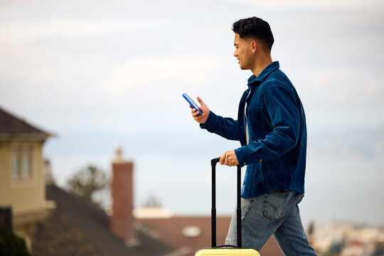 Man crosses the street, pulling a suitcase.