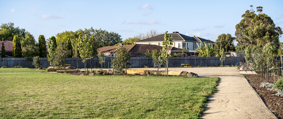 Open green space or a dog park in a suburban residential neighborhood in Australia with lawn, pedestrian pathway, and houses in the background. © Doublelee
