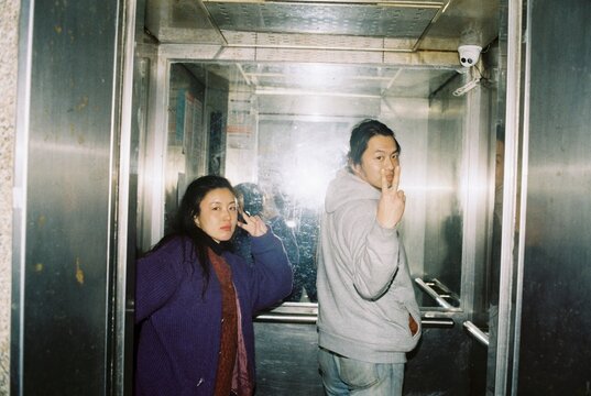 Asian couple in an elevator giving peace signs to the camera. 