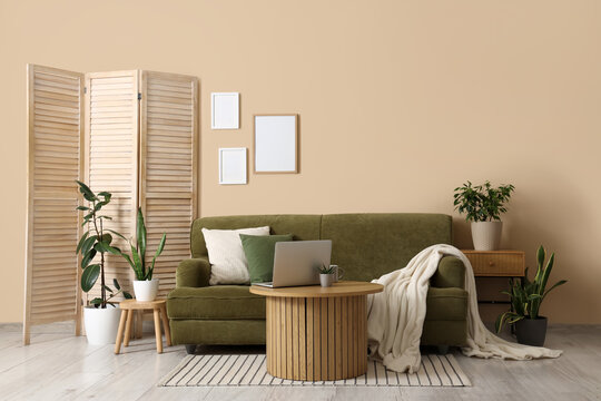 Interior of cozy living room with green sofa, folding screen and plants