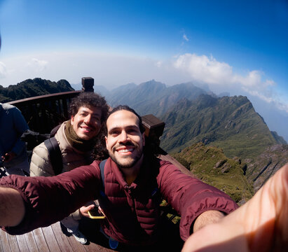 Two travelers taking selfie on mountain viewpoint deck