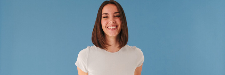 Beautiful brunette young woman dressed in white top looking at camera and smiling widely isolated...