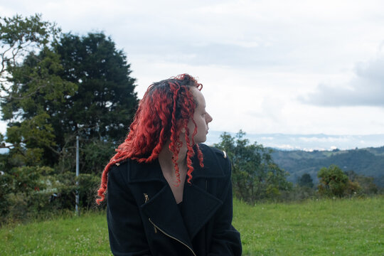 Woman With Curly Hair Sitting in a Green Field on a Cloudy Day