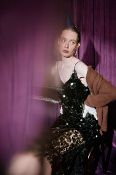 Portrait woman in sequin dress with party hat against purple backdrop