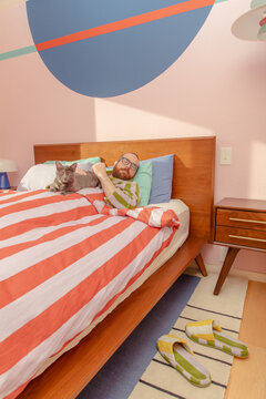 Man lounges in bed with cat