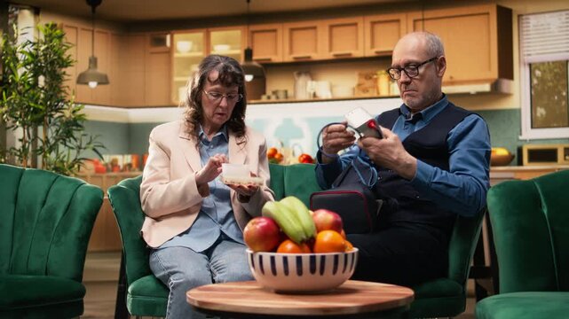 Two retirees, daily prescribed pills, monitoring blood pressure, BP monitor, old couple doing in-home medical routine with treatment and vital signs measurements for prevention. Quality of life.