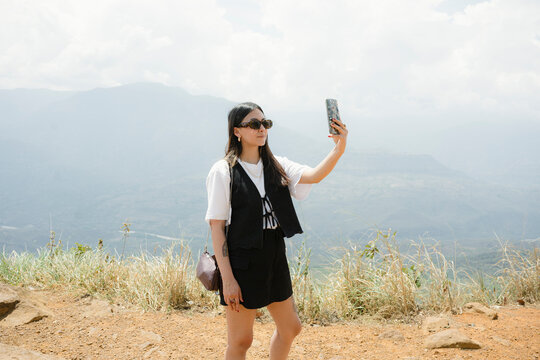 Woman taking selfie with phone on mountain viewpoint