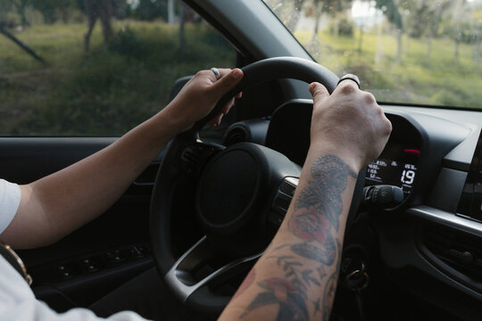 Man driving car with tattooed arm handling steering wheel
