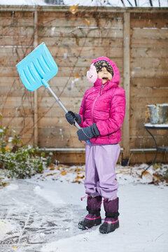 Child in pink puffer jacket and purple snow pants shovels snow